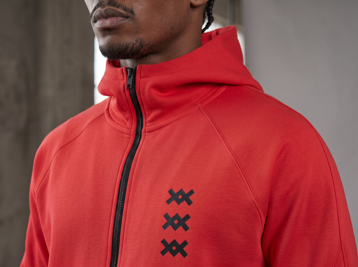 Detalle de la chaqueta del tracksuit AMV rojo con cierre negro y logos AMV en el pecho